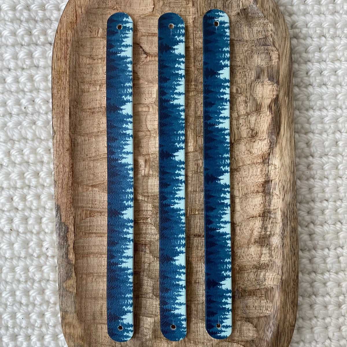 Vue de dessus à plat de trois bandes en biothane pour collier de chien, ornées d'un motif interchangeable chien élégant aux nuances de bleu représentant une forêt de conifères.