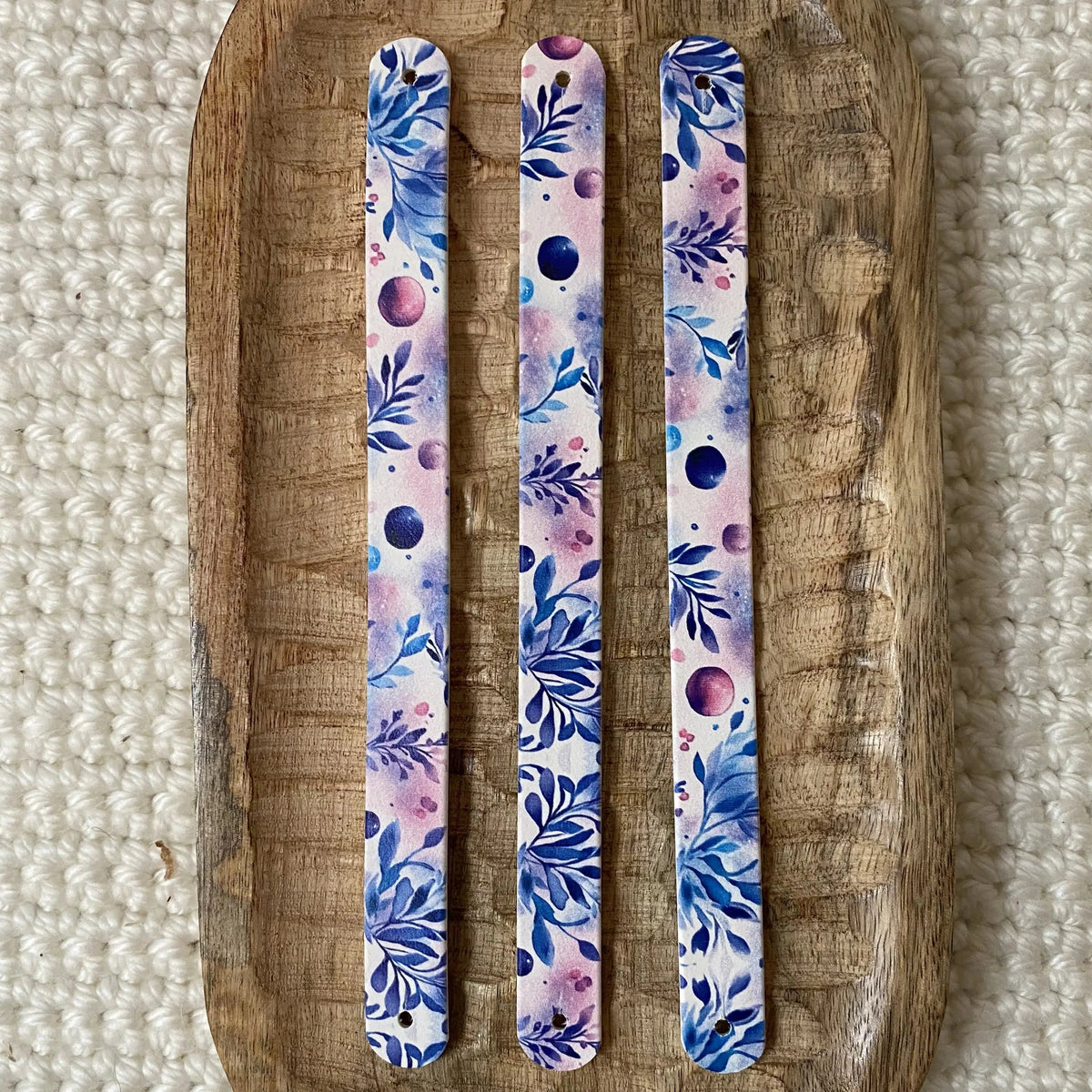Vue de dessus à plat de trois bandes en biothane pour collier de chien, illustrées d'un motif interchangeable chien artistique aux feuilles bleues et touches d'aquarelle mauves sur fond clair.