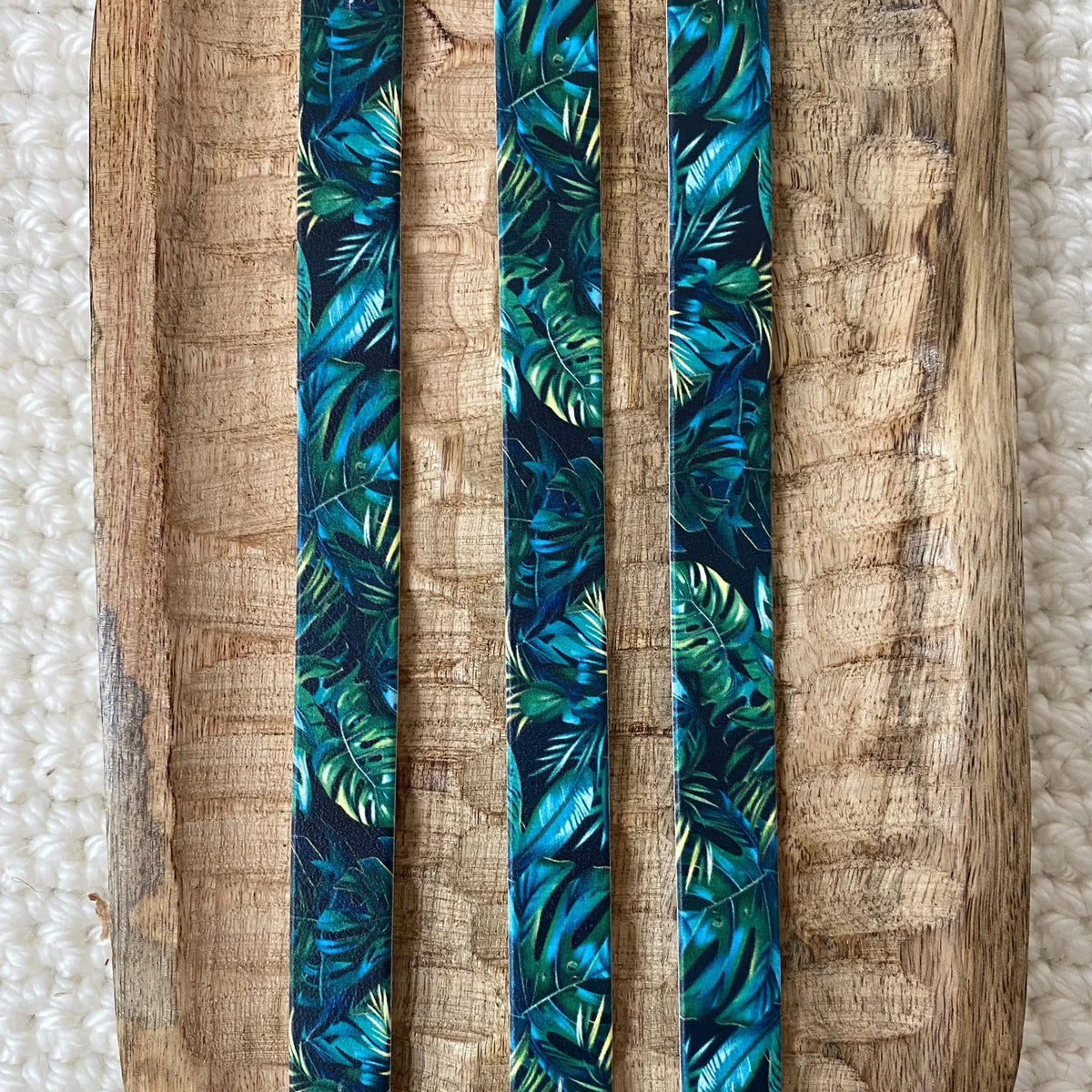 Vue de dessus à plat de trois bandes en biothane pour collier de chien, imprimées d'un motif interchangeable chien tropical sombre aux feuilles de palmiers et monstera vert profond et turquoise.