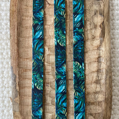 Vue de dessus à plat de trois bandes en biothane pour collier de chien, imprimées d'un motif interchangeable chien tropical sombre aux feuilles de palmiers et monstera vert profond et turquoise.