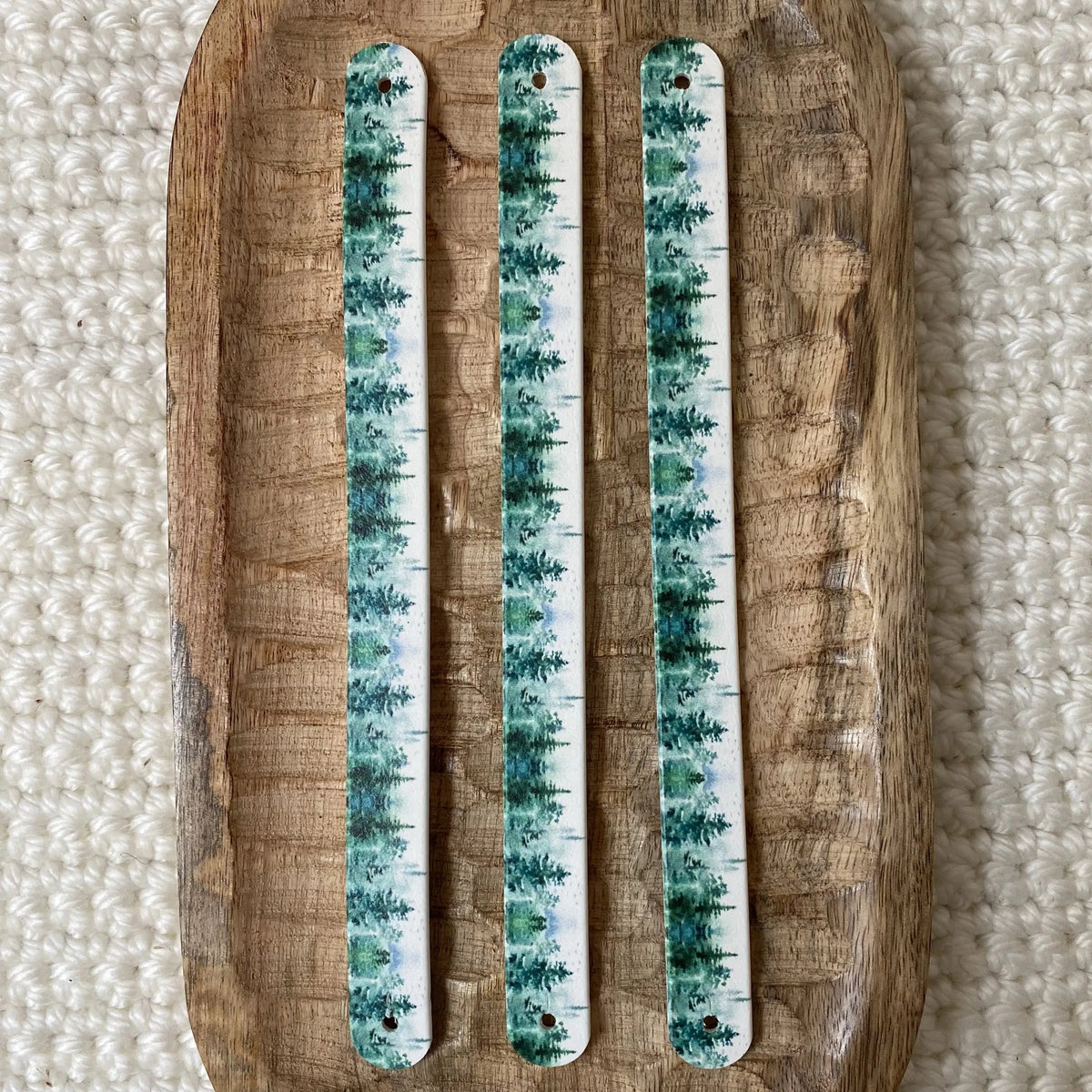 Vue de dessus à plat de trois bandes en biothane pour collier de chien, décorées d'un motif interchangeable chien végétal de conifères et pins aquarelle verts et turquoise sur fond lumineux.