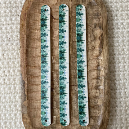 Vue de dessus à plat de trois bandes en biothane pour collier de chien, décorées d'un motif interchangeable chien végétal de conifères et pins aquarelle verts et turquoise sur fond lumineux.