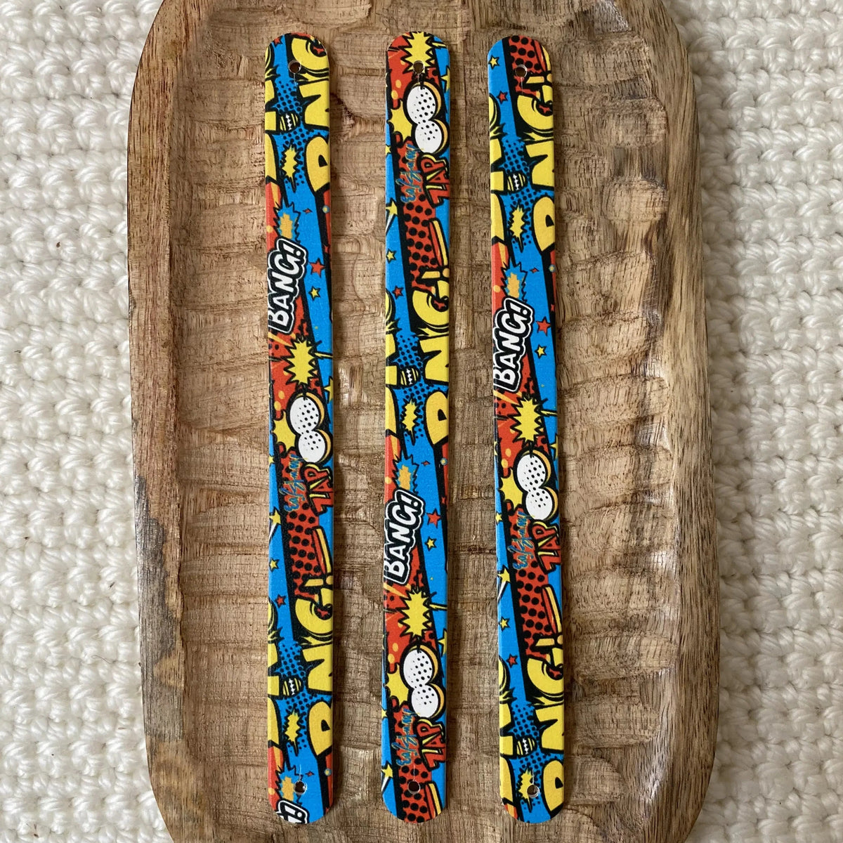 Vue de dessus à plat de trois bandes en biothane pour collier de chien, présentant un motif interchangeable chien BD coloré aux bulles d'action et graphismes pop art sur fond bleu.