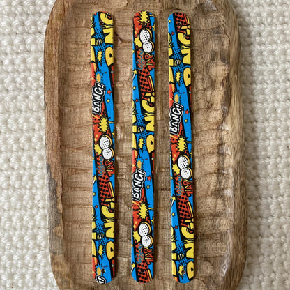 Vue de dessus à plat de trois bandes en biothane pour collier de chien, présentant un motif interchangeable chien BD coloré aux bulles d'action et graphismes pop art sur fond bleu.