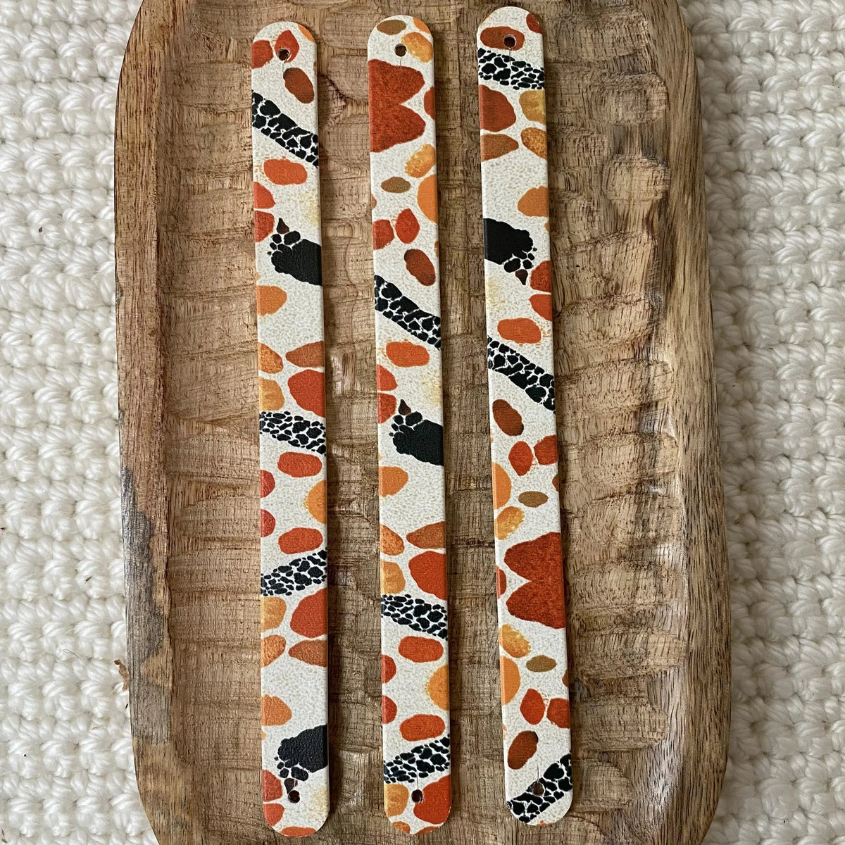 Vue de dessus à plat de trois bandes en biothane pour collier de chien, décorées d'un motif interchangeable chien animalier aux taches terracotta, orange et détails noirs sur fond neutre.