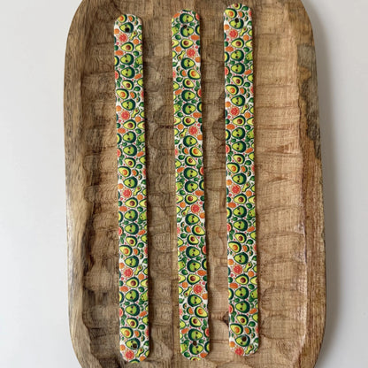 Vue de dessus de trois bandes à motifs interchangeables pour collier de chien en sangle étanche, motif petits avocats rigolos, présentées sur un plateau en bois sculpté.