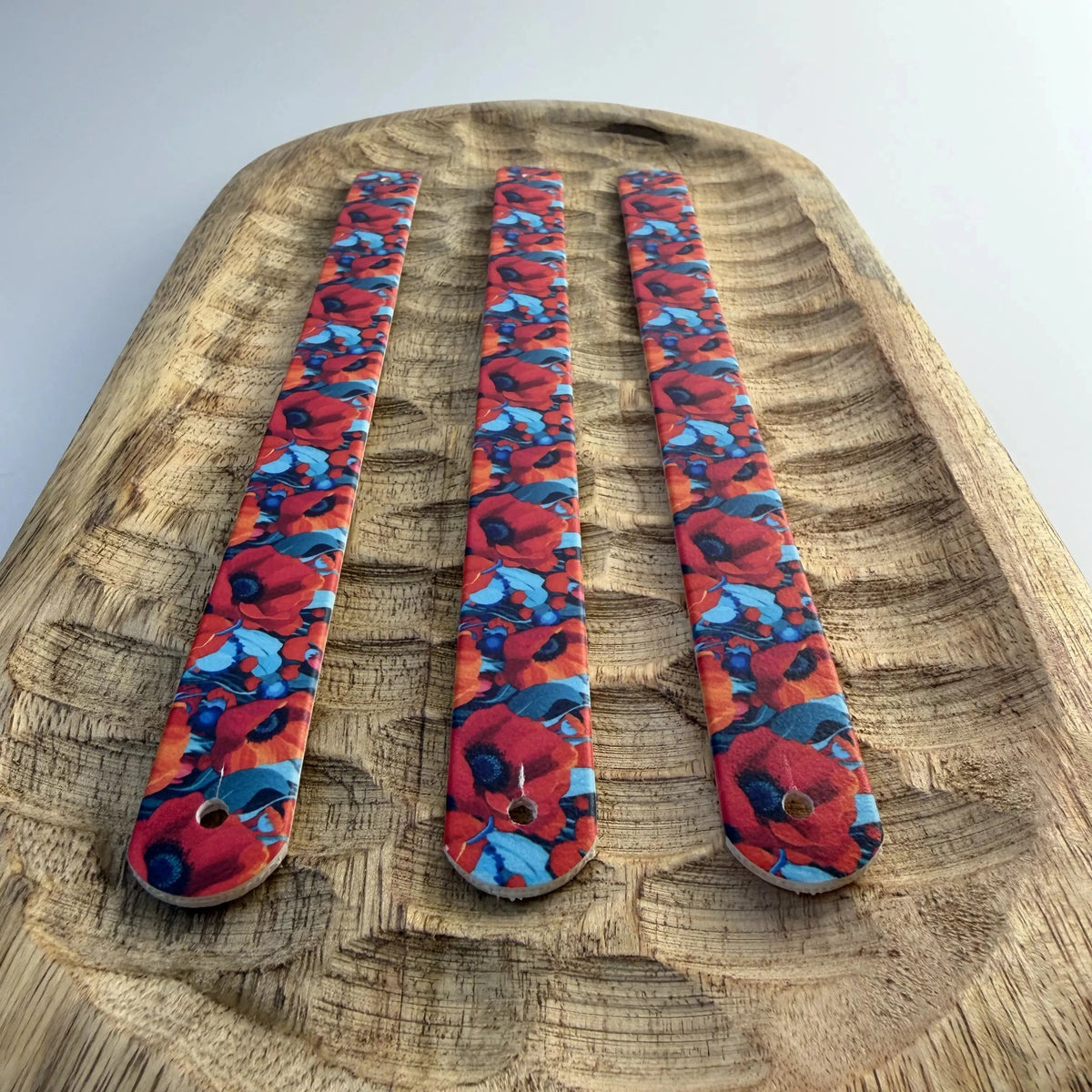 Vue de dessus de trois bandes à motifs interchangeables pour collier de chien en sangle étanche, motif floral coquelicots rouges et bleus, présentées sur un plateau en bois sculpté.