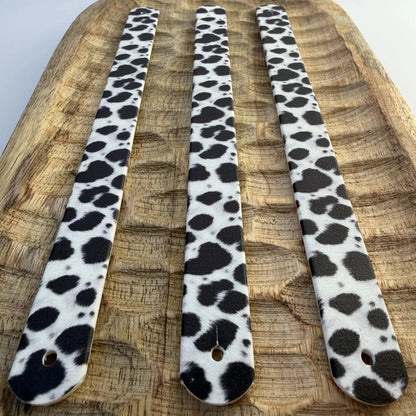 Vue de dessus de trois bandes à motifs interchangeables pour collier de chien en sangle étanche, motif taches de dalmatien noir et blanc, présentées sur un plateau en bois sculpté.