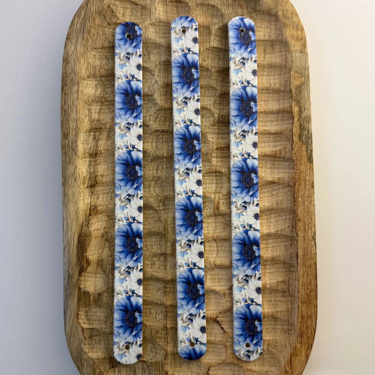 Vue de dessus de trois bandes à motifs interchangeables pour collier de chien en sangle étanche, motif floral bleu et blanc, présentées sur un plateau en bois sculpté.