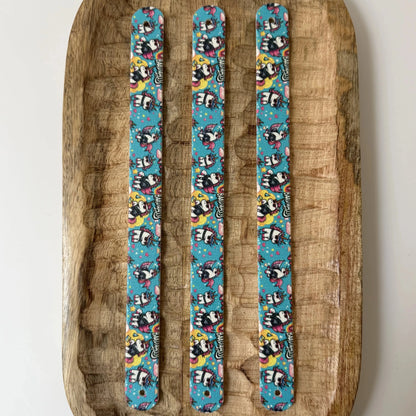 Vue de dessus de trois bandes à motifs interchangeables pour collier de chien en sangle étanche, motif licornes rock avec lunettes de soleil sur fond bleu turquoise, présentées sur un plateau en bois sculpté.