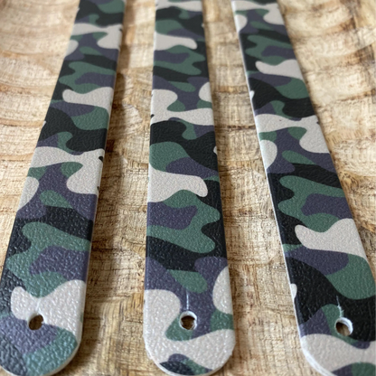 Perspective rapprochée de trois sangles en biothane sur plateau en bois, arborant un motif interchangeable chien camouflage militaire classique aux teintes de vert, kaki, noir et beige.
