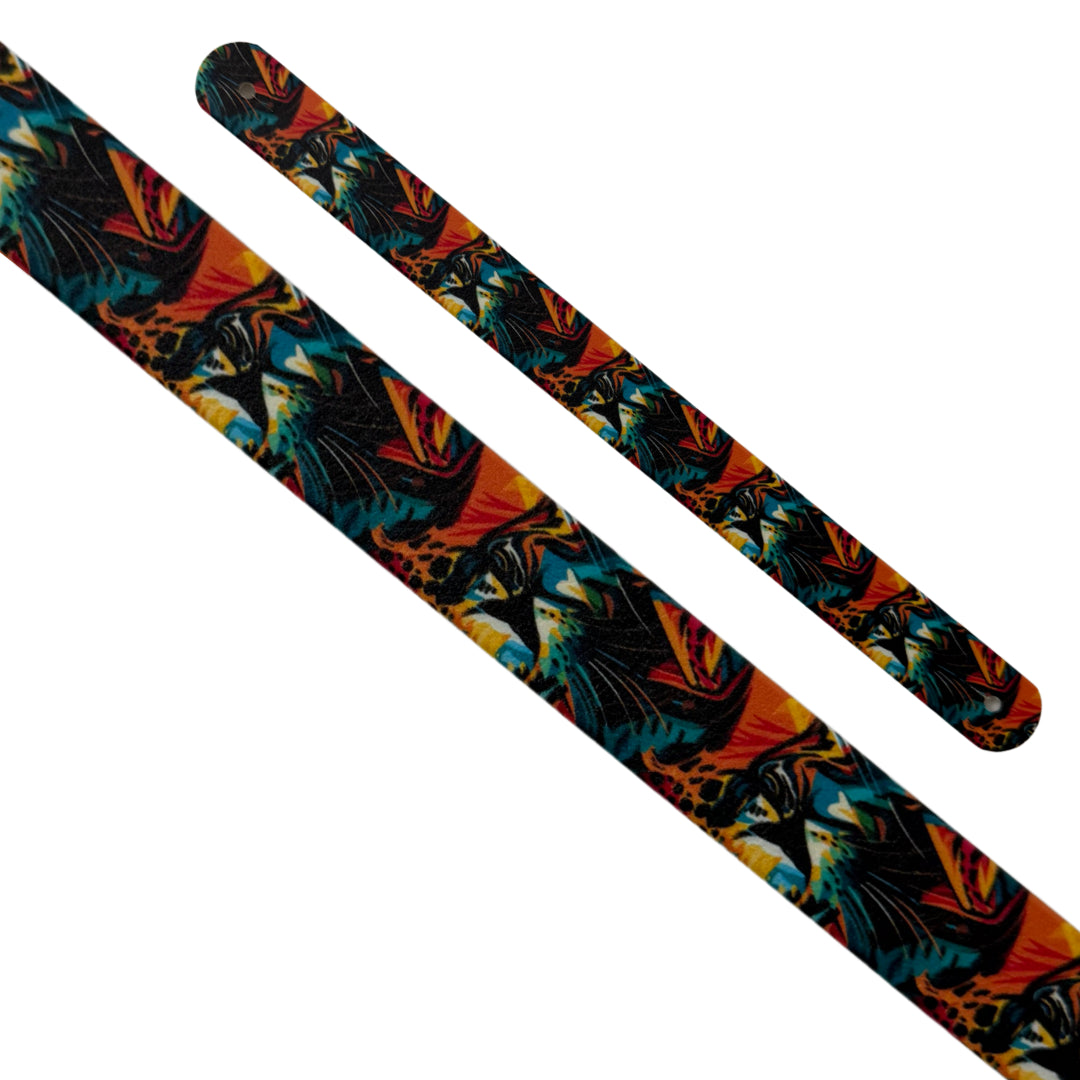 Gros plan en diagonale sur deux sangles interchangeables en biothane sur fond blanc. Le motif représente un mélange abstrait et coloré de motifs animaliers (léopard et peut-être zèbre) et de formes félines noires stylisées, dans des tons d'orange brûlé, de bleu canard et de noir. Les extrémités perforées sont visibles.