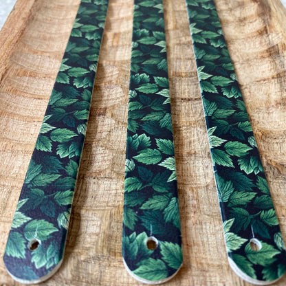 Perspective rapprochée de trois sangles en biothane sur bois texturé, décorées d'un motif interchangeable chien botanique représentant un feuillage dense aux multiples nuances de vert.