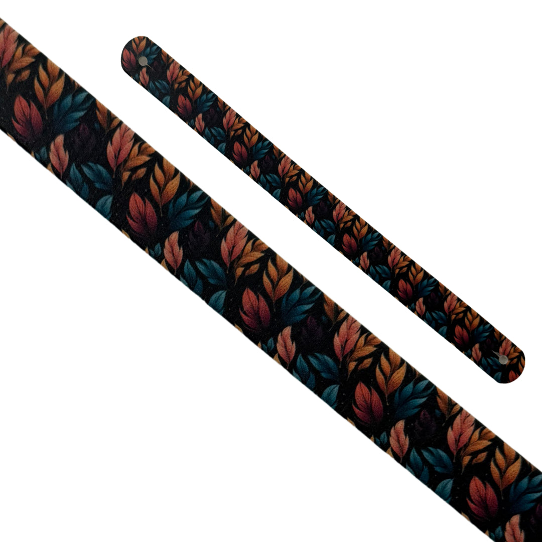 Gros plan en diagonale sur deux sangles interchangeables en biothane sur fond blanc. Les sangles présentent le motif "Forêt Crépusculaire", un imprimé détaillé de feuillage aux couleurs automnales (bleu sarcelle, orange brûlé, rose) sur un fond noir. Les extrémités perforées sont bien visibles.