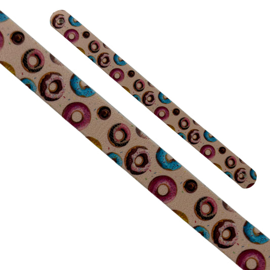 Gros plan en diagonale sur deux sangles interchangeables en biothane sur fond blanc. Le motif "Gourmandise Sucrée" est un imprimé amusant et coloré de beignets (donuts) avec des glaçages roses, bleus et au chocolat sur fond beige. Les extrémités perforées sont visibles.