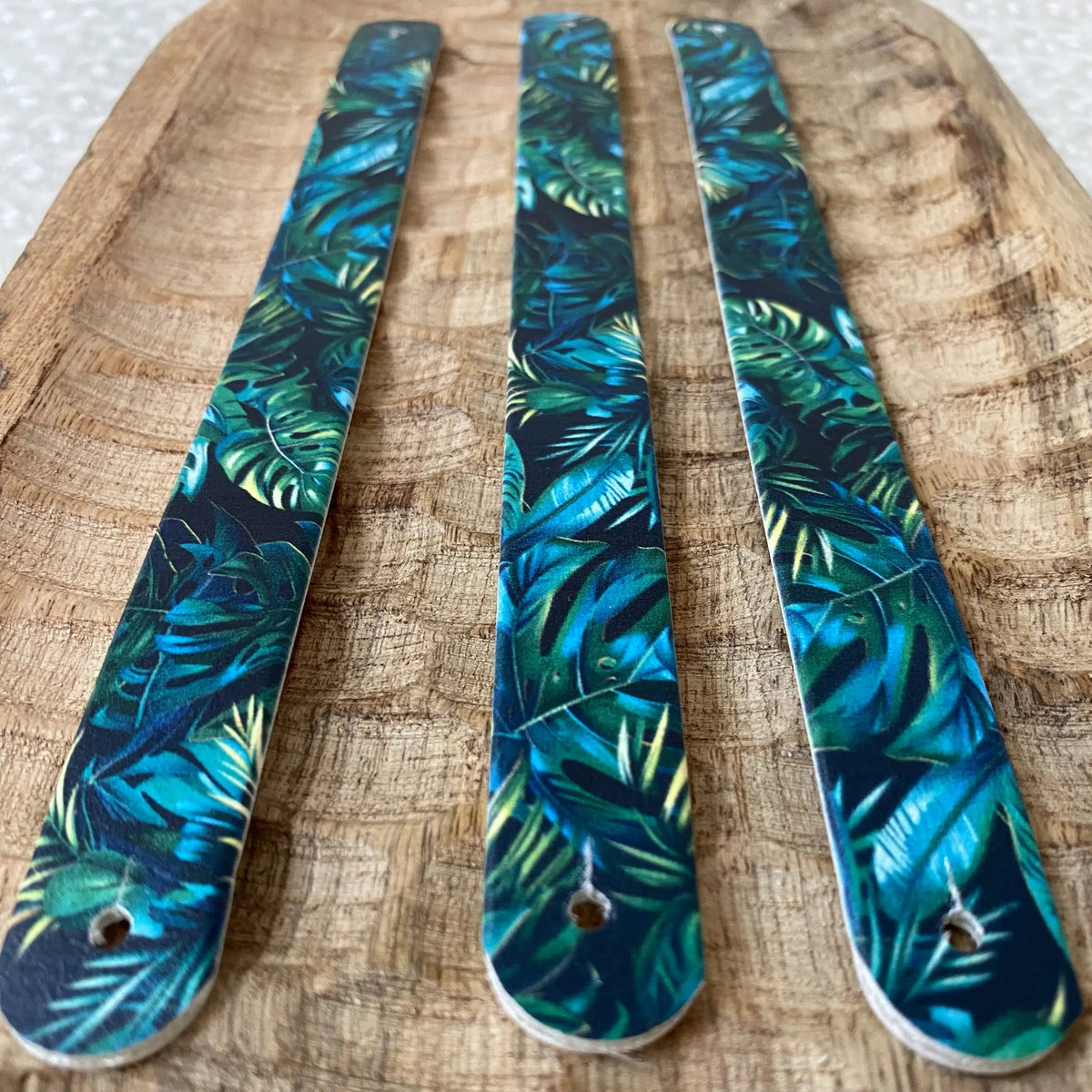 Perspective rapprochée de trois sangles en biothane sur fond bois. Le motif interchangeable chien jungle luxuriante met en scène de denses feuilles de monstera vert émeraude et bleu nuit sur fond noir.