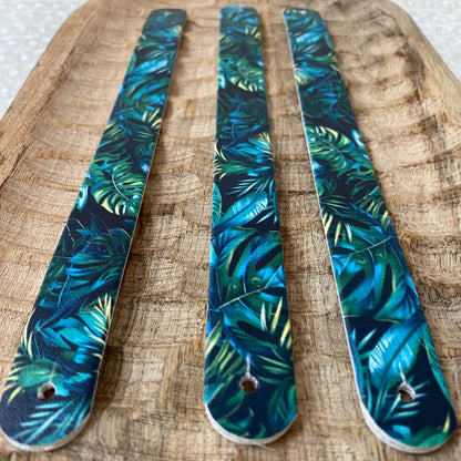 Perspective rapprochée de trois sangles en biothane sur fond bois. Le motif interchangeable chien jungle luxuriante met en scène de denses feuilles de monstera vert émeraude et bleu nuit sur fond noir.