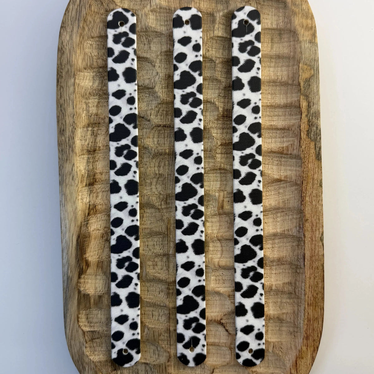 trois bandes à motifs interchangeables pour collier de chien en sangle étanche, motif taches de dalmatien noir et blanc, présentées sur un plateau en bois sculpté.