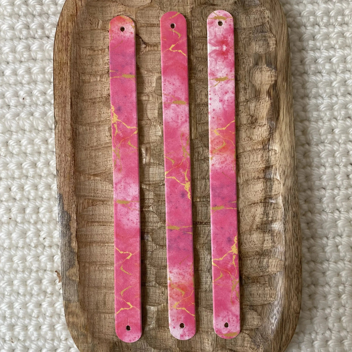 Vue à plat de dessus de trois bandes en biothane pour collier de chien, imprimées d'un motif interchangeable chien élégant façon marbre rose et d'éclats dorés sur plateau en bois.