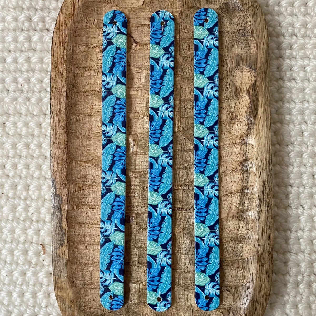 Vue à plat de dessus de trois bandes en biothane pour collier de chien, présentant un motif interchangeable chien exotique de denses palmes bleues et vert d'eau sur fond bleu nuit.