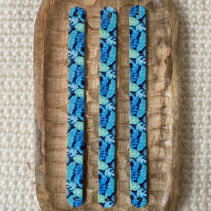 Vue à plat de dessus de trois bandes en biothane pour collier de chien, présentant un motif interchangeable chien exotique de denses palmes bleues et vert d'eau sur fond bleu nuit.