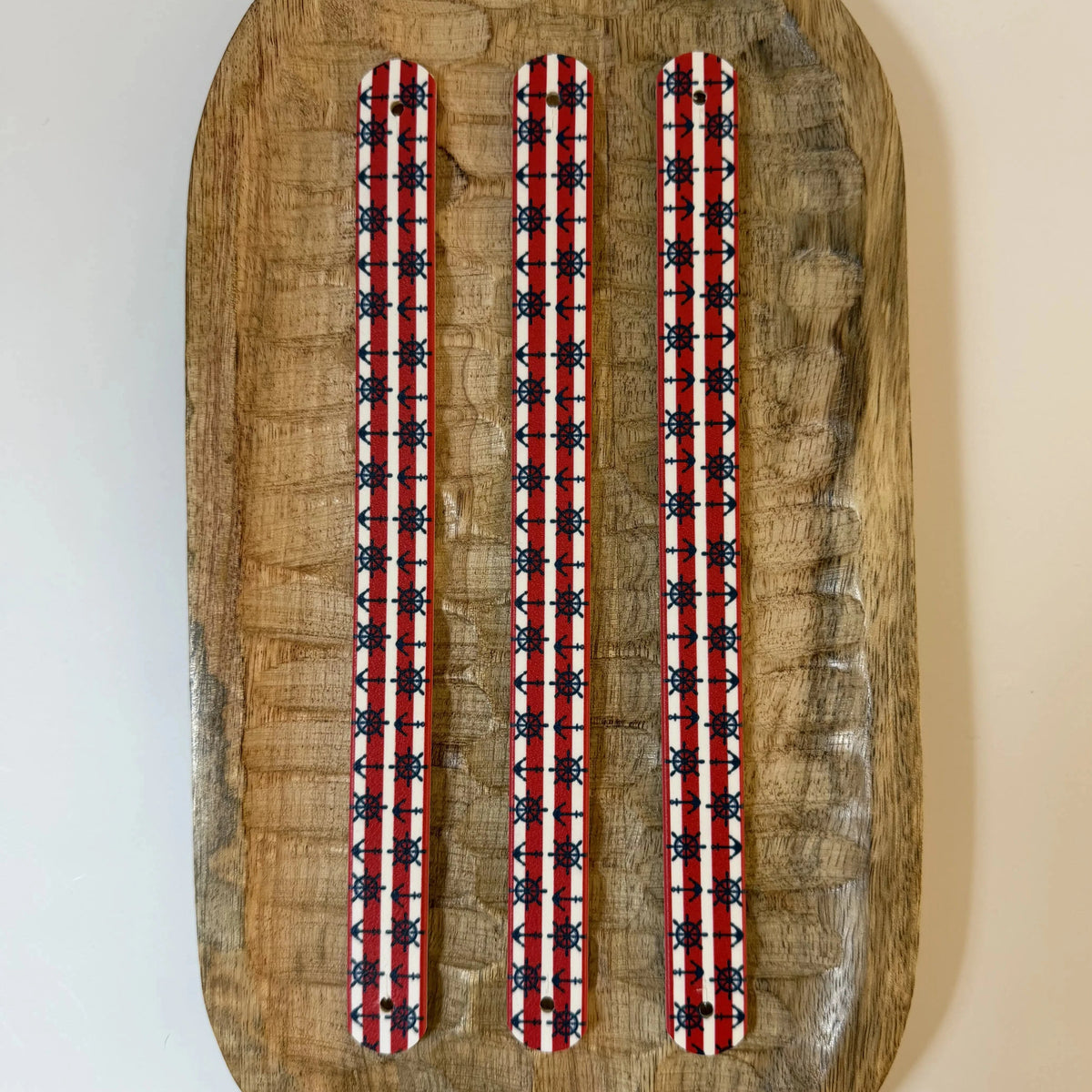 Vue à plat de dessus de trois sangles en biothane pour collier de chien, imprimées d'un motif interchangeable chien nautique classique avec rayures rouges et blanches, ancres et gouvernails bleu marine, posées sur du bois.