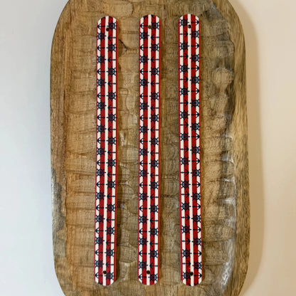 Vue à plat de dessus de trois sangles en biothane pour collier de chien, imprimées d'un motif interchangeable chien nautique classique avec rayures rouges et blanches, ancres et gouvernails bleu marine, posées sur du bois.