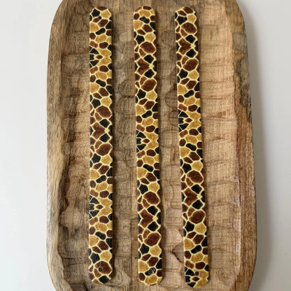 bandes à motifs interchangeables pour collier de chien en sangle étanche, motif peau de girafe à taches marron et ocre, posées sur un plateau en bois sculpté.