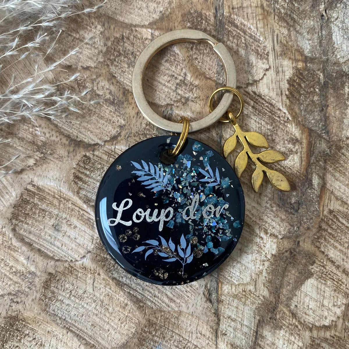 Détail des motifs botaniques bleus et des reflets pailletés sur résine noire