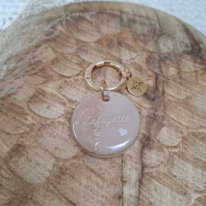 Médaille personnalisée pour chien en résine aux tons nude et dorés posée sur un support en bois